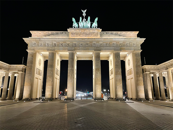 A grand neoclassical German monument is lighted at night. Atop the monument sits a sculpture of a chariot drawn by four horses.